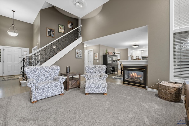 carpeted living area with a high ceiling, stairway, a multi sided fireplace, and baseboards