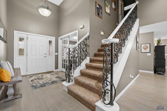 foyer entrance featuring a towering ceiling, stairs, baseboards, and wood finished floors