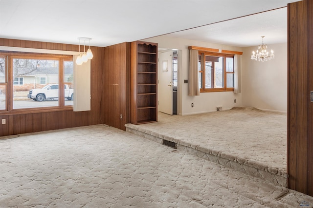 spare room featuring wood walls, carpet, visible vents, and a notable chandelier