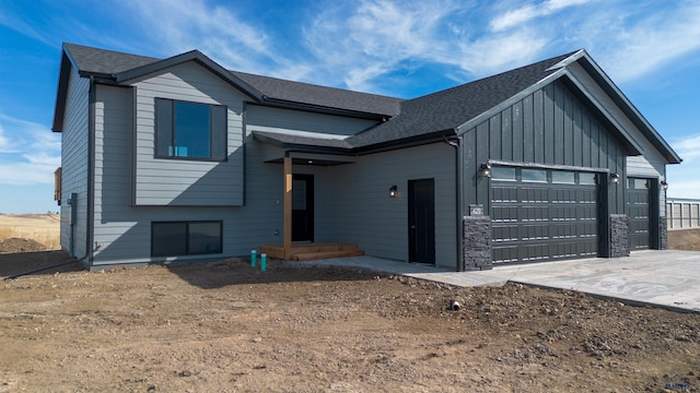 view of front of house featuring an attached garage, driveway, stone siding, roof with shingles, and board and batten siding