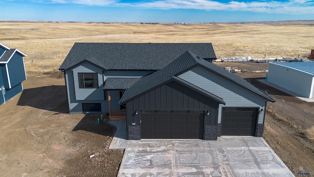 view of front facade featuring a garage, a shingled roof, driveway, stone siding, and board and batten siding