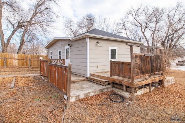 rear view of property featuring a deck, a shingled roof, and fence