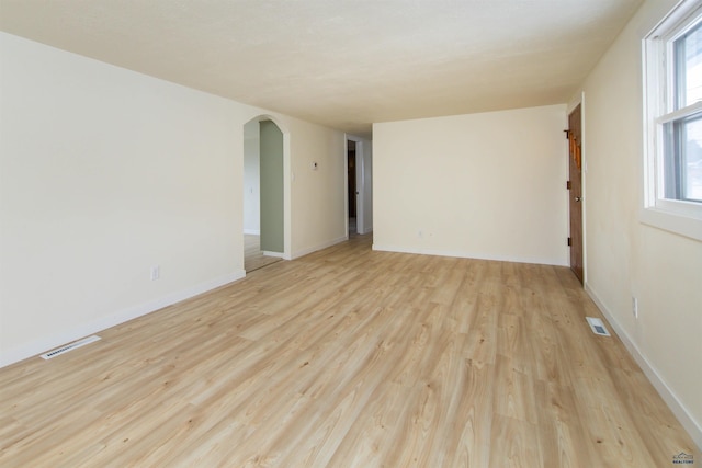 spare room featuring arched walkways, baseboards, visible vents, and light wood finished floors