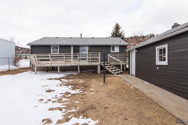 snow covered back of property featuring a shingled roof, a wooden deck, and fence