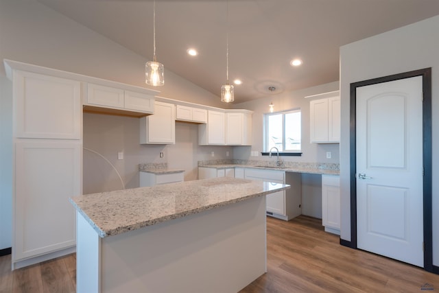 kitchen with light stone countertops, white cabinetry, a sink, and wood finished floors