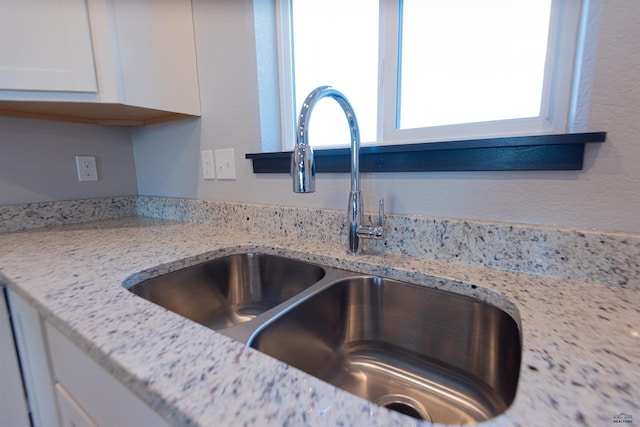 room details with light stone counters, a sink, and white cabinetry