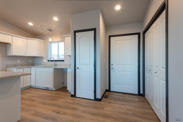 kitchen with light wood-style floors, a sink, light stone countertops, and white cabinets