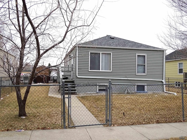 view of side of home with a fenced front yard, a gate, a shingled roof, and a lawn