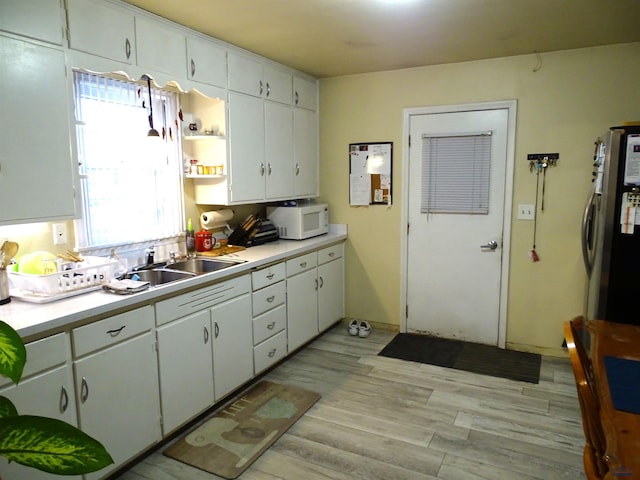 kitchen with light countertops, a sink, light wood finished floors, and white microwave