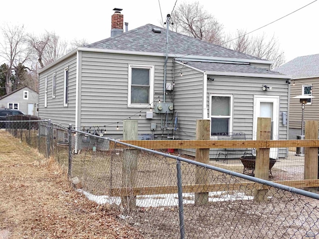 back of house with a shingled roof, a chimney, and fence