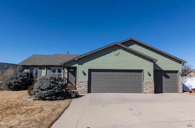 view of front of home with a garage, stone siding, a shingled roof, and concrete driveway