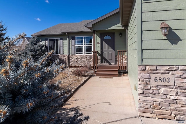 entrance to property featuring stone siding and roof with shingles