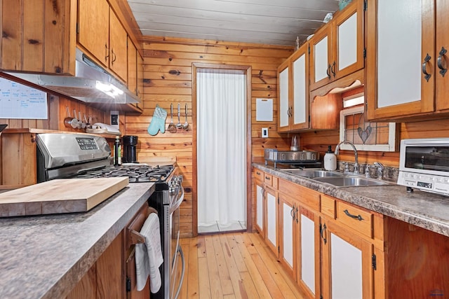 kitchen featuring dark countertops, a sink, wooden walls, and gas range