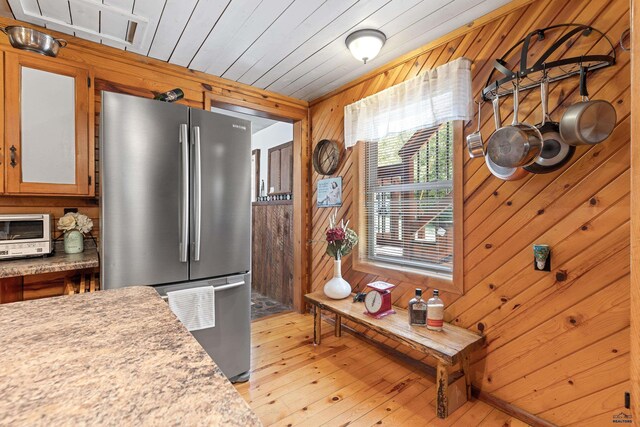 kitchen featuring light countertops, freestanding refrigerator, wooden walls, light wood-type flooring, and wooden ceiling