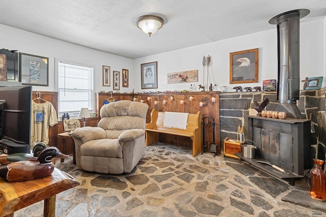 sitting room featuring a wood stove, a wainscoted wall, stone floors, and a textured ceiling