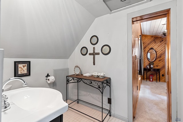 bathroom with lofted ceiling, wood walls, and a sink