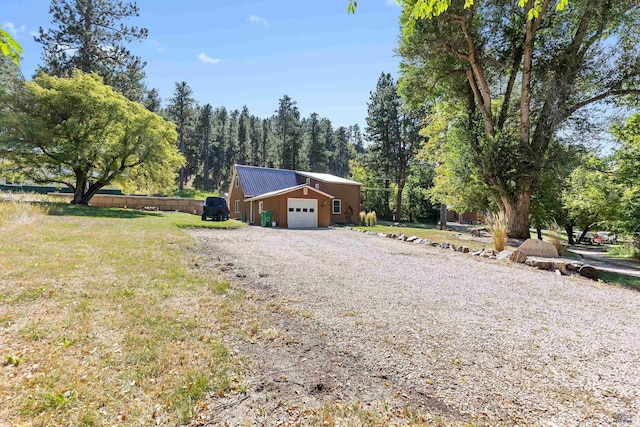 exterior space featuring a front lawn, gravel driveway, metal roof, and an attached garage