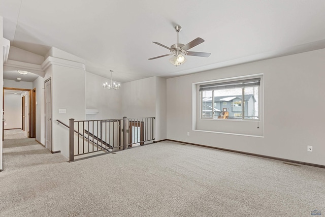 carpeted spare room featuring ceiling fan with notable chandelier and baseboards