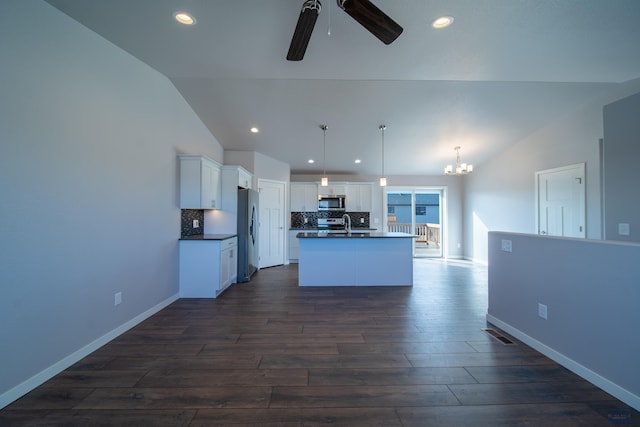 kitchen featuring dark wood finished floors, stainless steel appliances, dark countertops, decorative backsplash, and vaulted ceiling