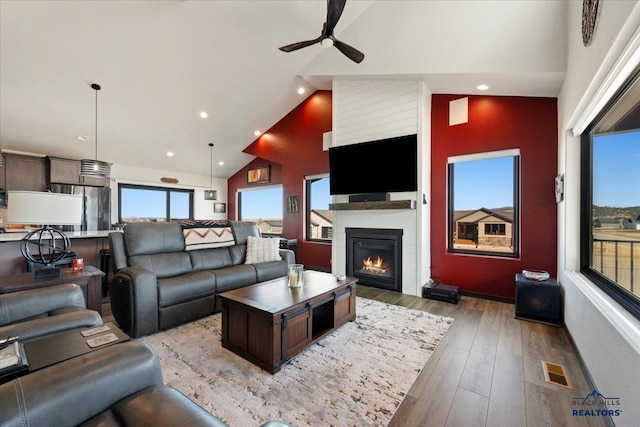 living area with high vaulted ceiling, a fireplace, wood finished floors, visible vents, and a ceiling fan