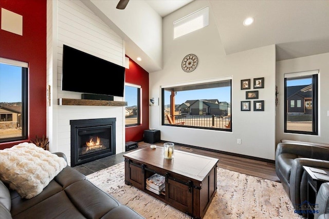 living area with baseboards, a towering ceiling, wood finished floors, a fireplace, and recessed lighting