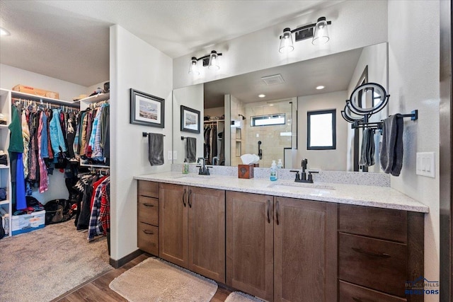 bathroom featuring double vanity, a stall shower, a sink, and wood finished floors