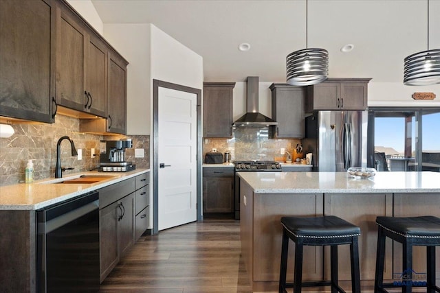 kitchen with dark wood finished floors, a kitchen bar, appliances with stainless steel finishes, a sink, and wall chimney exhaust hood