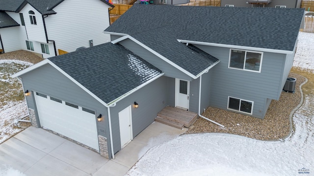 view of front of property with driveway, roof with shingles, an attached garage, and central air condition unit