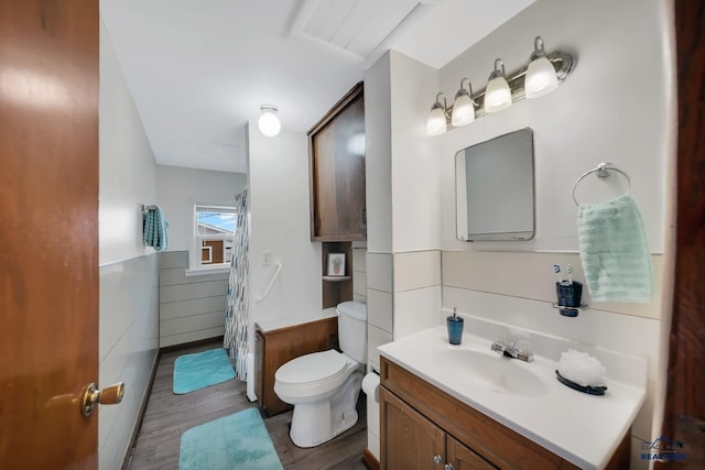 bathroom with a wainscoted wall, tile walls, toilet, vanity, and wood finished floors