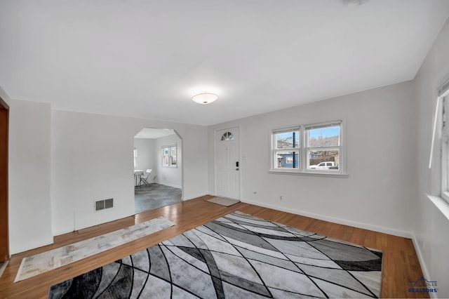 interior space with arched walkways, visible vents, baseboards, and wood finished floors