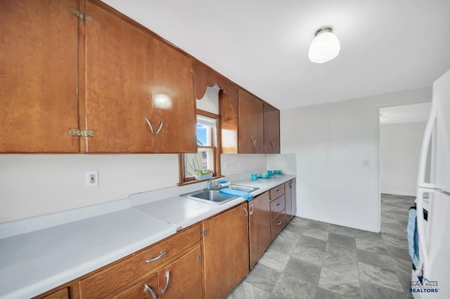 kitchen featuring brown cabinets, light countertops, freestanding refrigerator, a sink, and baseboards