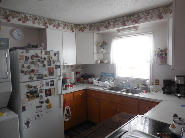 kitchen with stacked washer and dryer, freestanding refrigerator, light countertops, a textured ceiling, and a sink