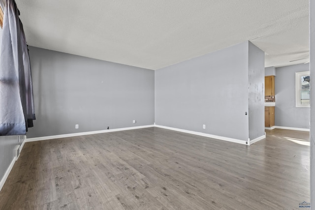 unfurnished living room with baseboards, a textured ceiling, and wood finished floors