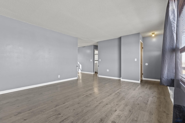 unfurnished living room with baseboards, a textured ceiling, and wood finished floors