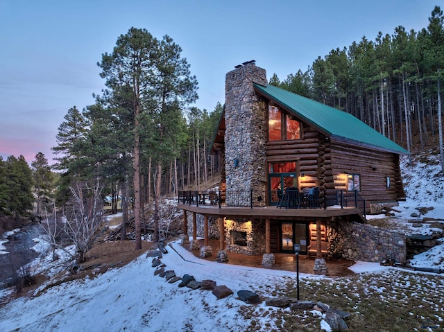 exterior space with log siding, a chimney, a deck, and metal roof