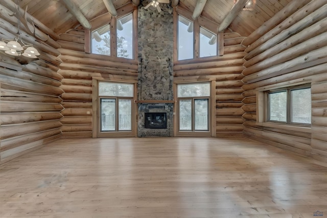 unfurnished living room featuring wood finished floors, a healthy amount of sunlight, beam ceiling, a stone fireplace, and wood ceiling