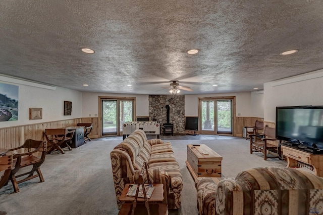 carpeted living room featuring plenty of natural light, wainscoting, a textured ceiling, and a wood stove