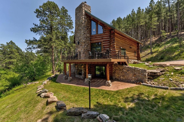 back of property featuring log exterior, a wooden deck, a lawn, a chimney, and a patio