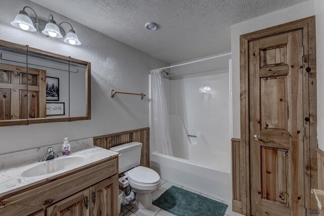 full bathroom with toilet, wainscoting, tile patterned floors, shower / bath combination with curtain, and a textured ceiling