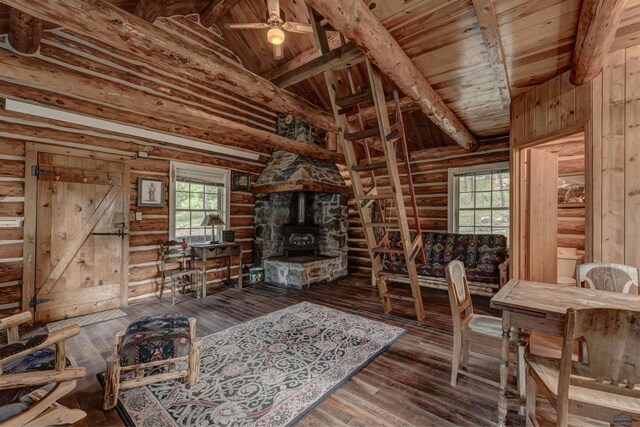 unfurnished living room with beamed ceiling, a healthy amount of sunlight, a wood stove, and hardwood / wood-style flooring