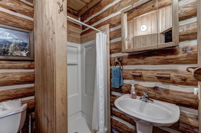 bathroom featuring toilet, a shower stall, log walls, and a sink