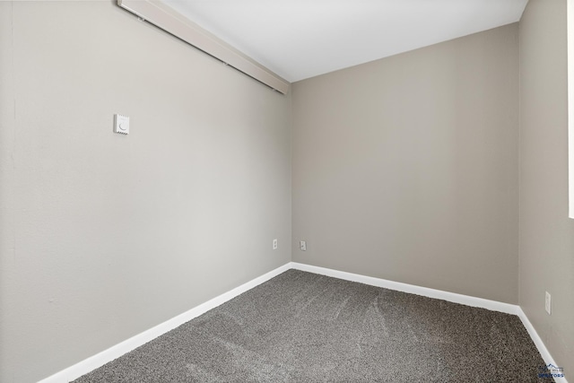 unfurnished room with baseboards and dark colored carpet