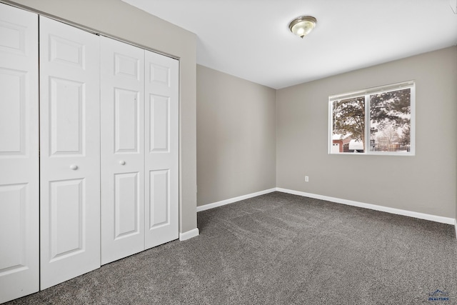 unfurnished bedroom featuring a closet, dark carpet, and baseboards