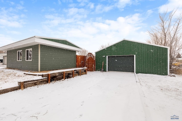 snow covered garage featuring a detached garage and fence