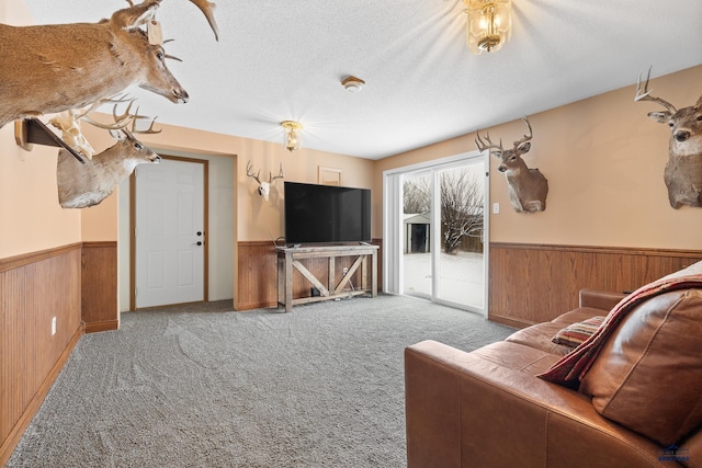 living area featuring wooden walls, a wainscoted wall, carpet floors, and a textured ceiling