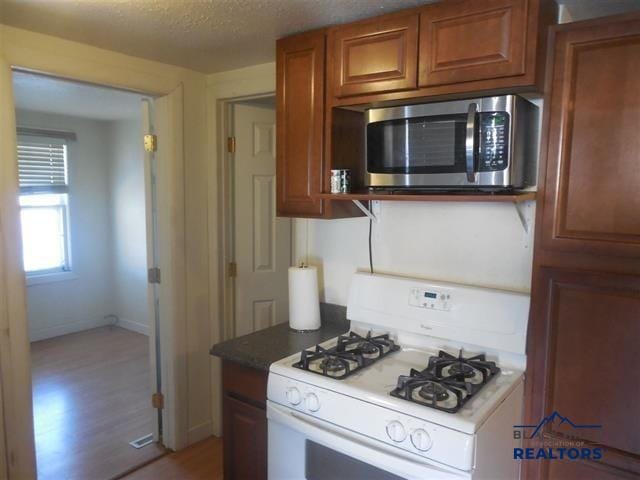 710 Haines Ave, Rapid City, SD 57701 - kitchen featuring brown cabinetry, white range with gas cooktop, light wood-style flooring, a textured ceiling, and stainless steel microwave