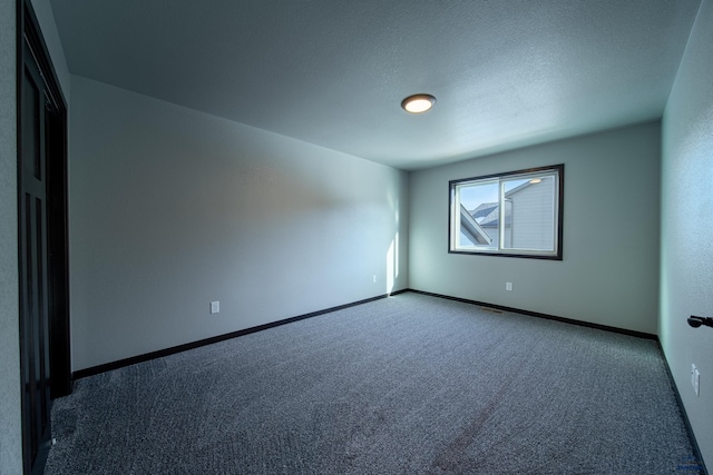 empty room with carpet flooring, baseboards, and a textured ceiling