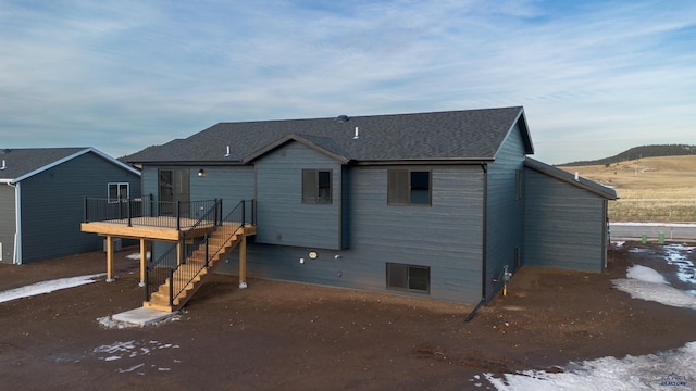 rear view of house with a deck, stairway, and roof with shingles