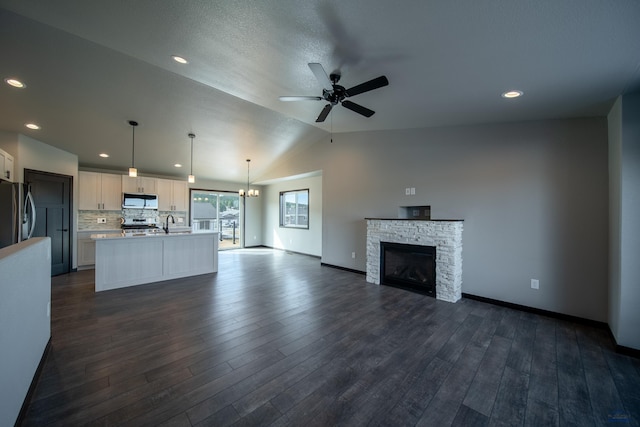 unfurnished living room featuring baseboards, lofted ceiling, a fireplace, dark wood-style flooring, and ceiling fan with notable chandelier