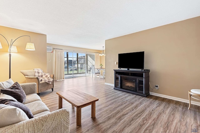 living area with a glass covered fireplace, a textured ceiling, baseboards, and wood finished floors